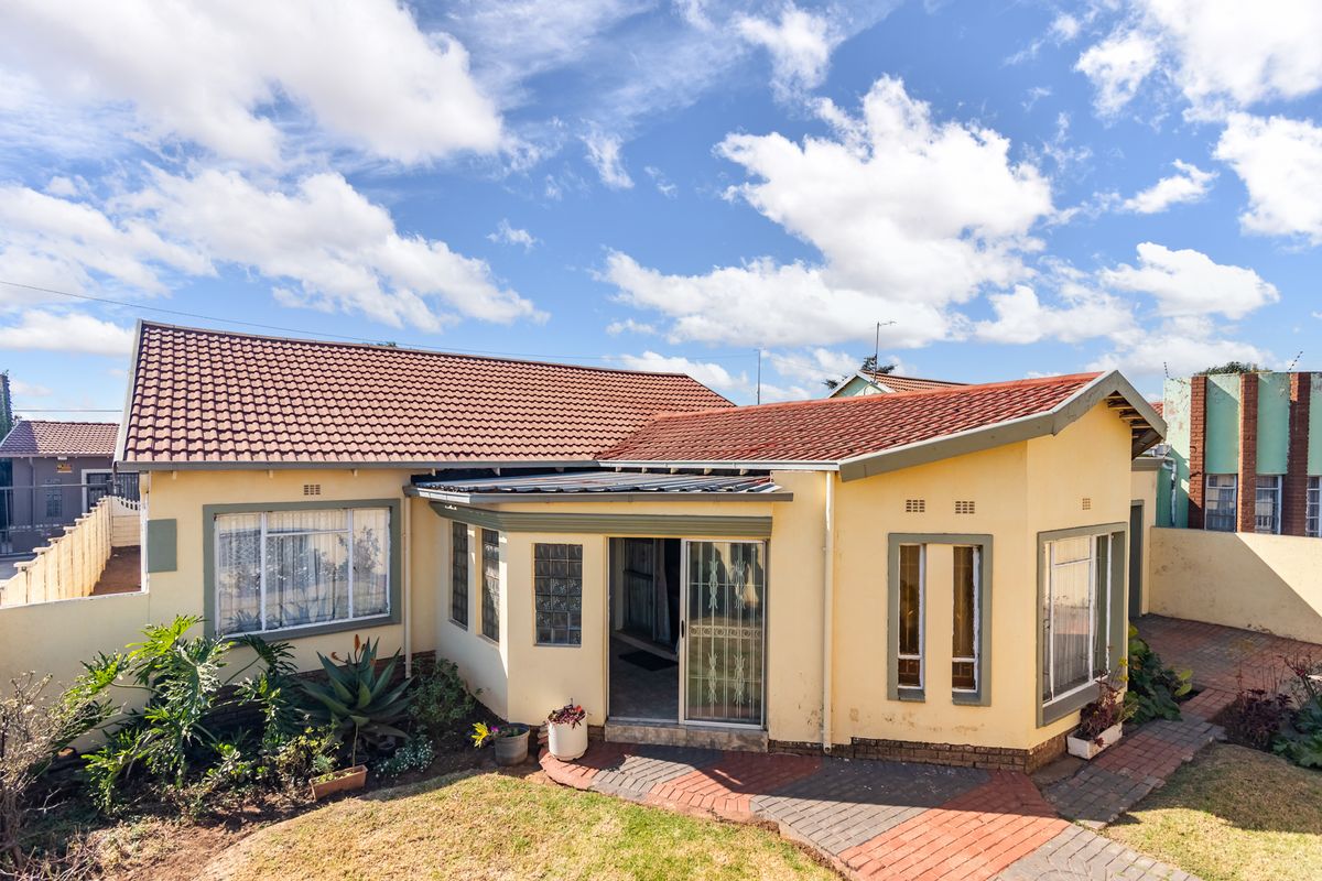 Rear view of the house featuring a tiled roof, brick paved patio area, and access through a sliding glass door with security gate.
