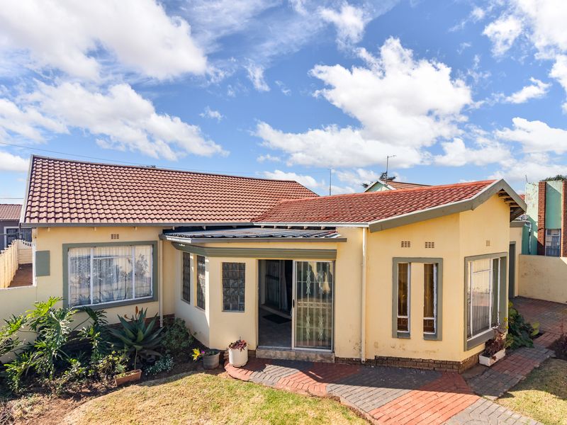 Rear view of the house featuring a tiled roof, brick paved patio area, and access through a sliding glass door with security gate.