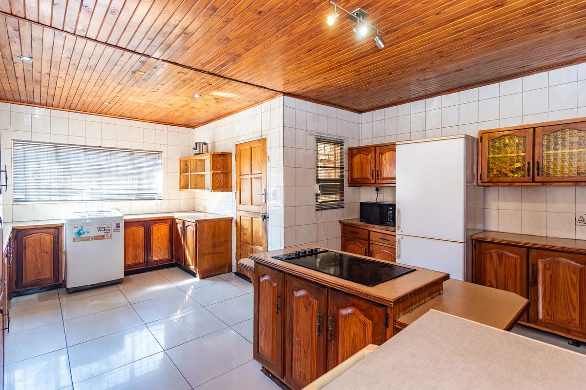 A spacious kitchen featuring wooden cabinetry, a central island with a built-in hob, tiled flooring, and a distinctive wooden ceiling.