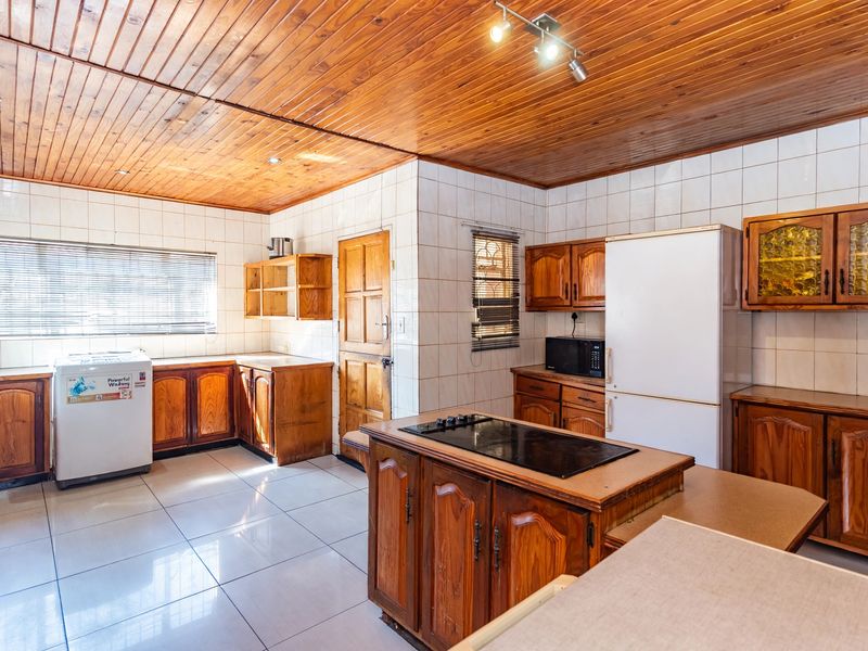 A spacious kitchen featuring wooden cabinetry, a central island with a built-in hob, tiled flooring, and a distinctive wooden ceiling.