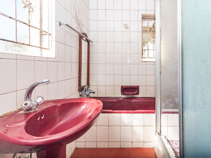 A dated bathroom featuring a red pedestal basin and matching bathtub, with white wall tiles and a separate shower enclosure.