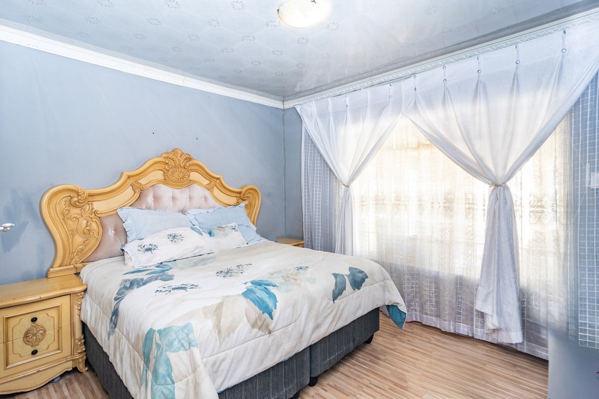 A bedroom featuring laminate flooring, decorative ceiling tiles, and crown molding. The room requires cosmetic updates to the wall finishes.