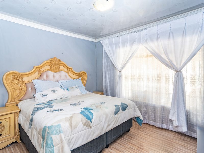 A bedroom featuring laminate flooring, decorative ceiling tiles, and crown molding. The room requires cosmetic updates to the wall finishes.