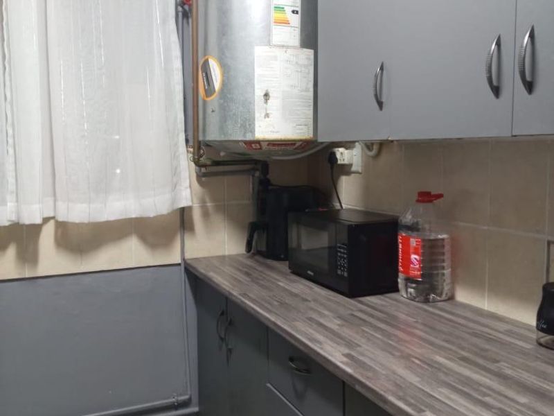 A functional scullery area featuring grey built-in cabinetry, laminate countertops, tiled backsplash, and an exposed electric water heater unit.