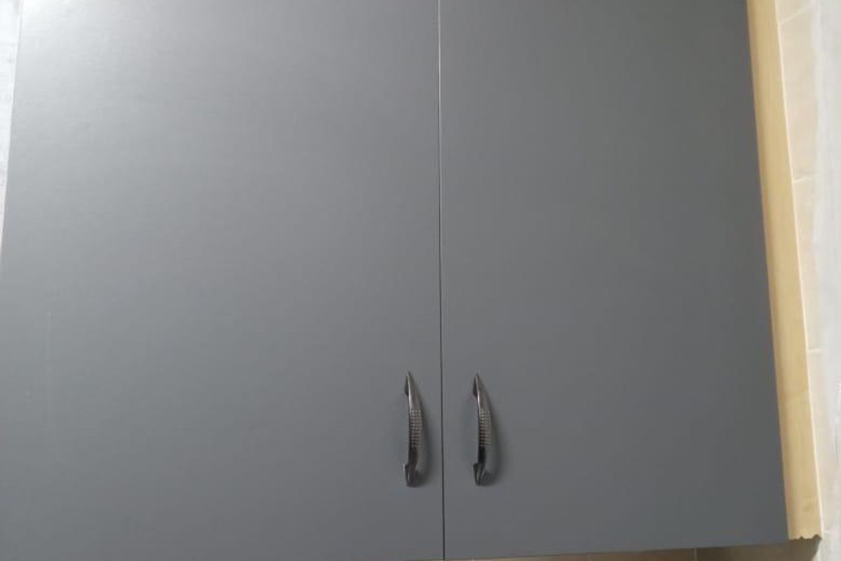 A close-up view of grey wall-mounted kitchen cabinetry with a tiled backsplash.