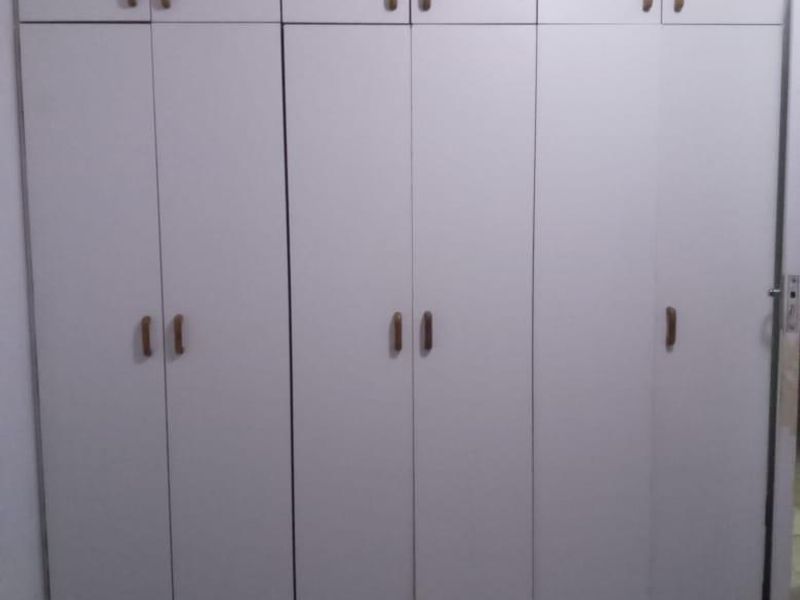 A bedroom featuring floor-to-ceiling white built-in cupboards with ample storage space and neutral tiled flooring.