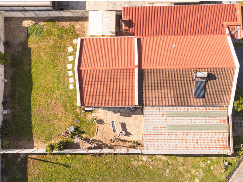 Aerial view of the property showing the main tiled roof, solar water heating system, rear paved patio area, and surrounding garden space.