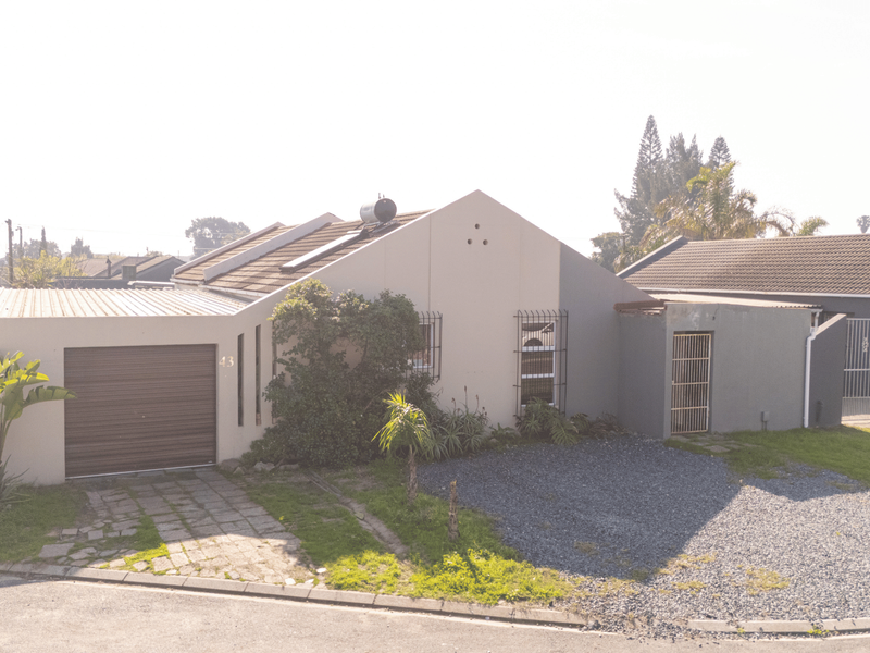 Front elevation of a single-story house featuring a garage, solar water heating system, and a combination of paved and gravel driveway areas.