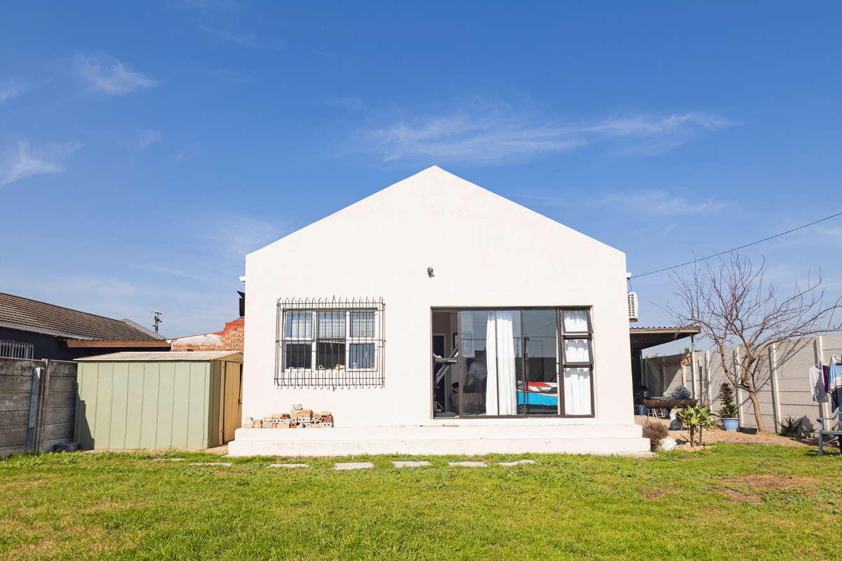 Rear view of the property featuring a white facade, sliding glass door with security bars, a metal storage shed, and a spacious garden area.