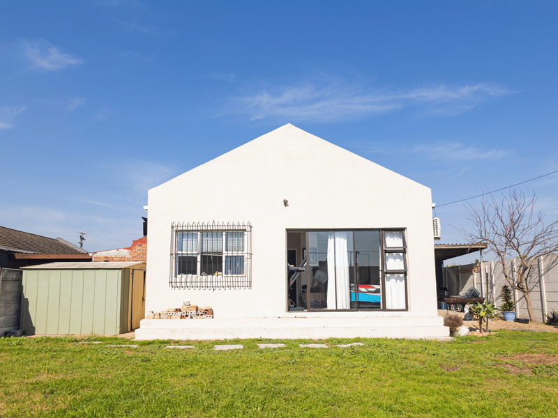 Rear view of the property featuring a white facade, sliding glass door with security bars, a metal storage shed, and a spacious garden area.