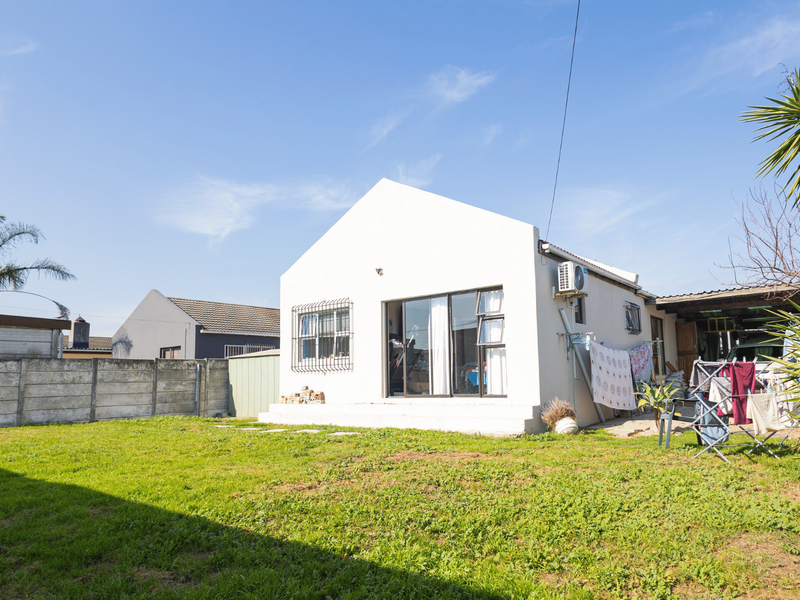 Rear view of the property featuring a white exterior facade, sliding glass doors, a concrete boundary wall, and a spacious grass garden area.