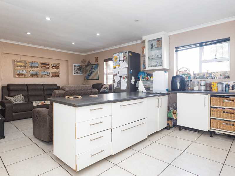 Open-plan living and kitchen area featuring a central island, tiled flooring, and ample built-in cabinetry, offering a functional and versatile living space.