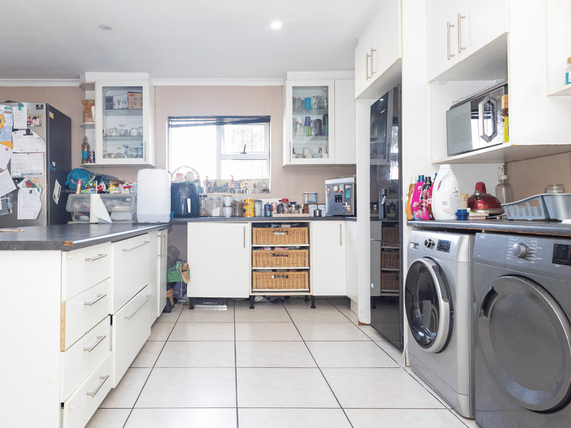 Functional kitchen featuring white cabinetry, laminate countertops, tiled flooring, and integrated laundry appliances, offering a practical layout with potential for cosmetic updates.