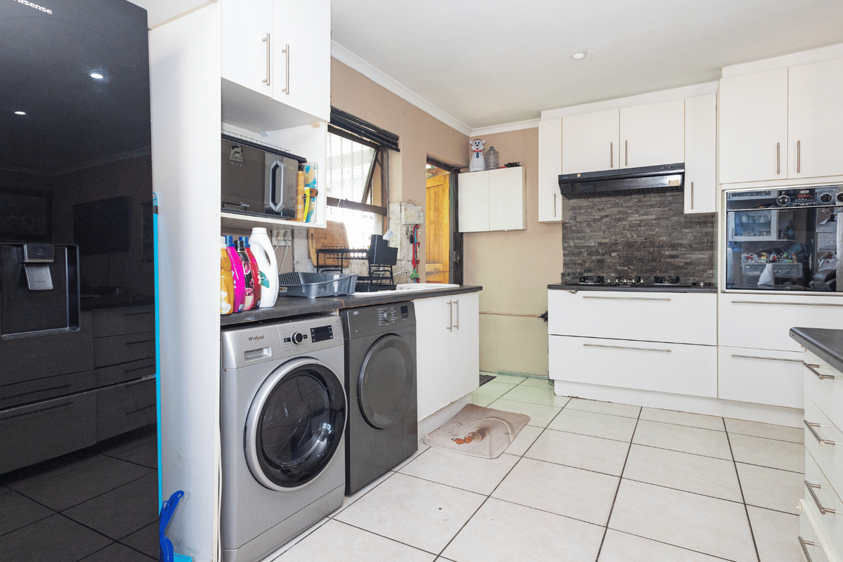 Functional kitchen featuring white cabinetry, built-in oven, gas hob, stone tile backsplash, and integrated laundry space with tiled flooring.