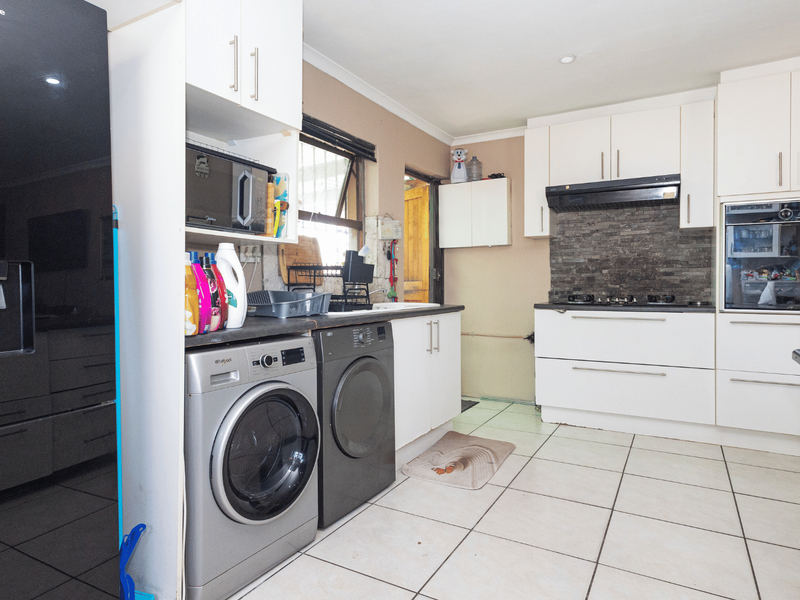 Functional kitchen featuring white cabinetry, built-in oven, gas hob, stone tile backsplash, and integrated laundry space with tiled flooring.