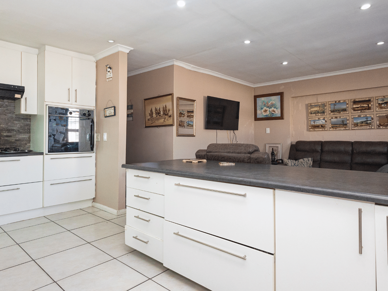 Open-plan kitchen and living area featuring a central island, built-in oven, gas hob, and stone tile flooring.