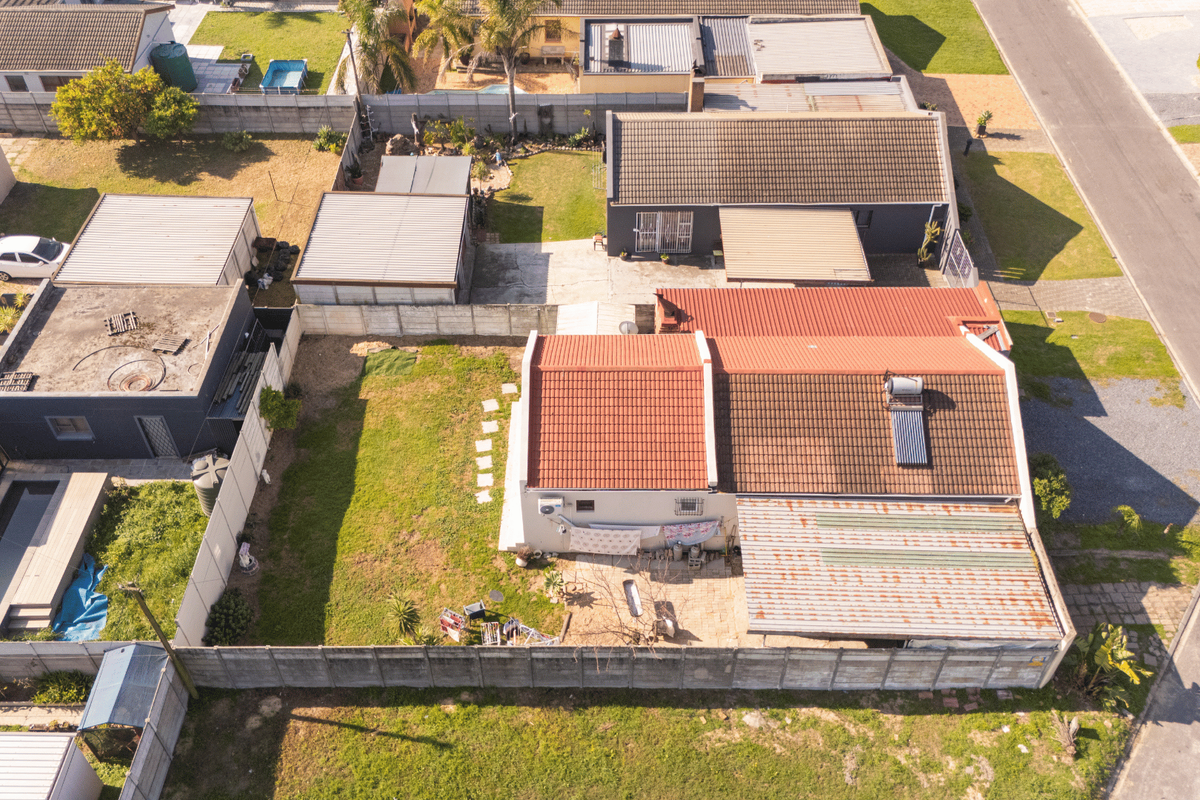 Aerial view of the property showing the main dwelling with a tiled roof, solar water heater, rear garden, and surrounding residential neighborhood.