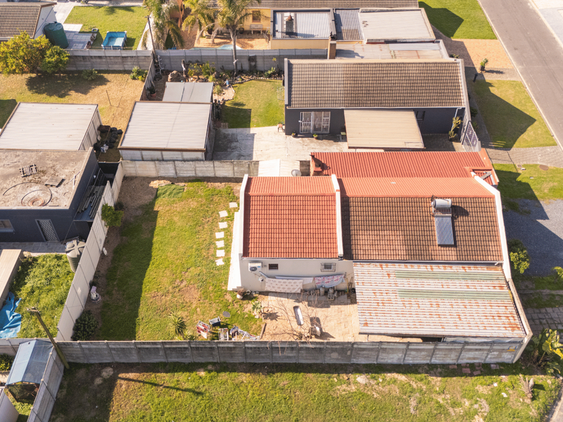 Aerial view of the property showing the main dwelling with a tiled roof, solar water heater, rear garden, and surrounding residential neighborhood.