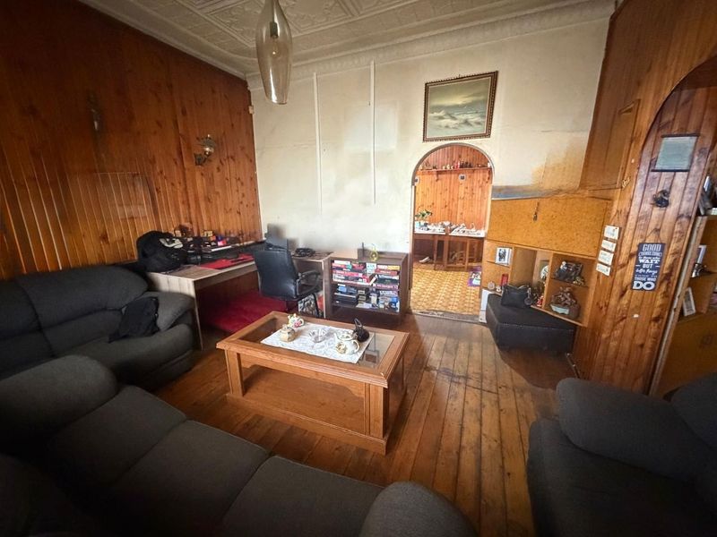 A living room featuring traditional timber wall paneling, a decorative pressed metal ceiling, and original timber flooring, leading through an arched doorway to another space.