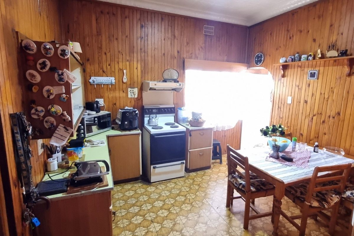 A dated kitchen featuring timber wall paneling, original cabinetry, and a freestanding stove, offering significant potential for a modern renovation.