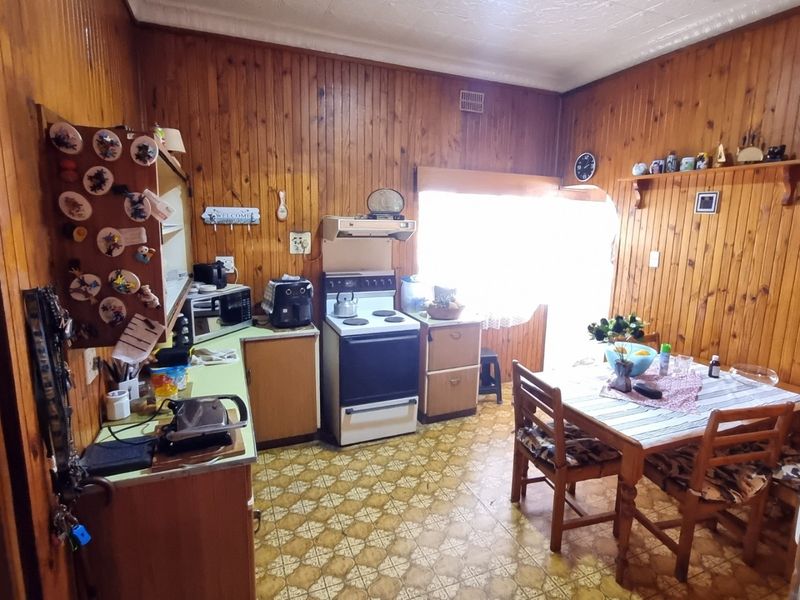 A dated kitchen featuring timber wall paneling, original cabinetry, and a freestanding stove, offering significant potential for a modern renovation.