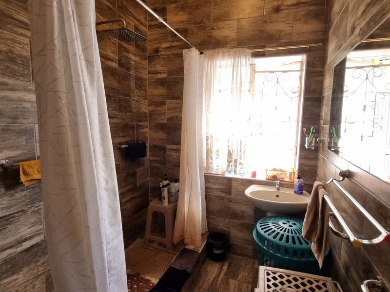 A compact bathroom featuring wood-look wall and floor tiles, a pedestal basin, and a walk-in shower area with a rain shower head.