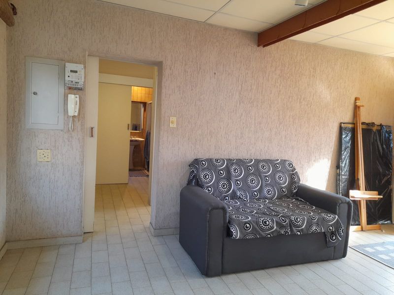 Living area featuring tiled flooring, textured walls, and an exposed ceiling beam, with direct access to an adjoining bathroom.