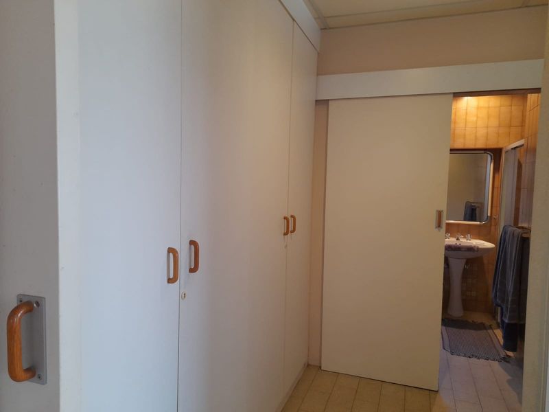 A hallway featuring extensive built-in storage cupboards and a sliding door providing access to an adjacent bathroom with a pedestal basin.