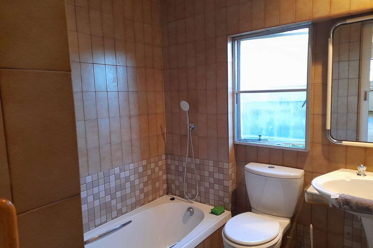 A functional bathroom featuring a built-in bathtub with a handheld shower, pedestal sink, and full-height ceramic wall tiling.