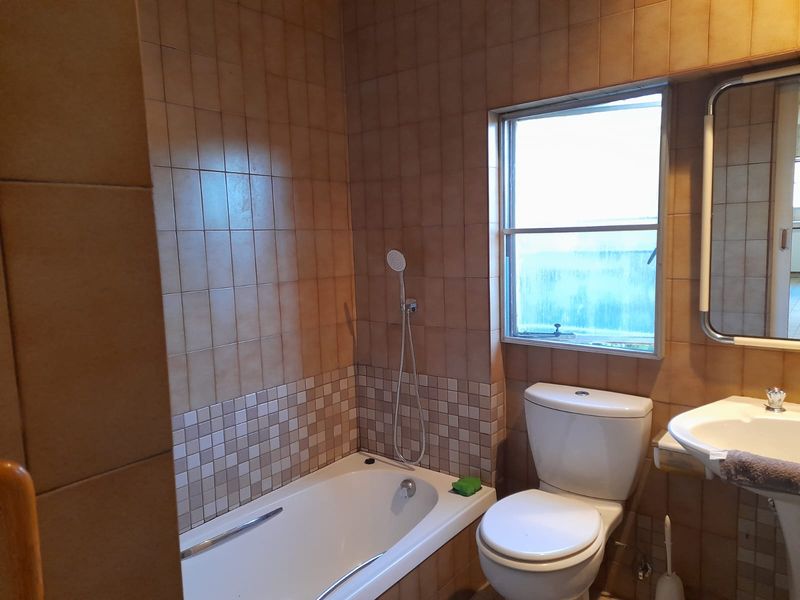 A functional bathroom featuring a built-in bathtub with a handheld shower, pedestal sink, and full-height ceramic wall tiling.