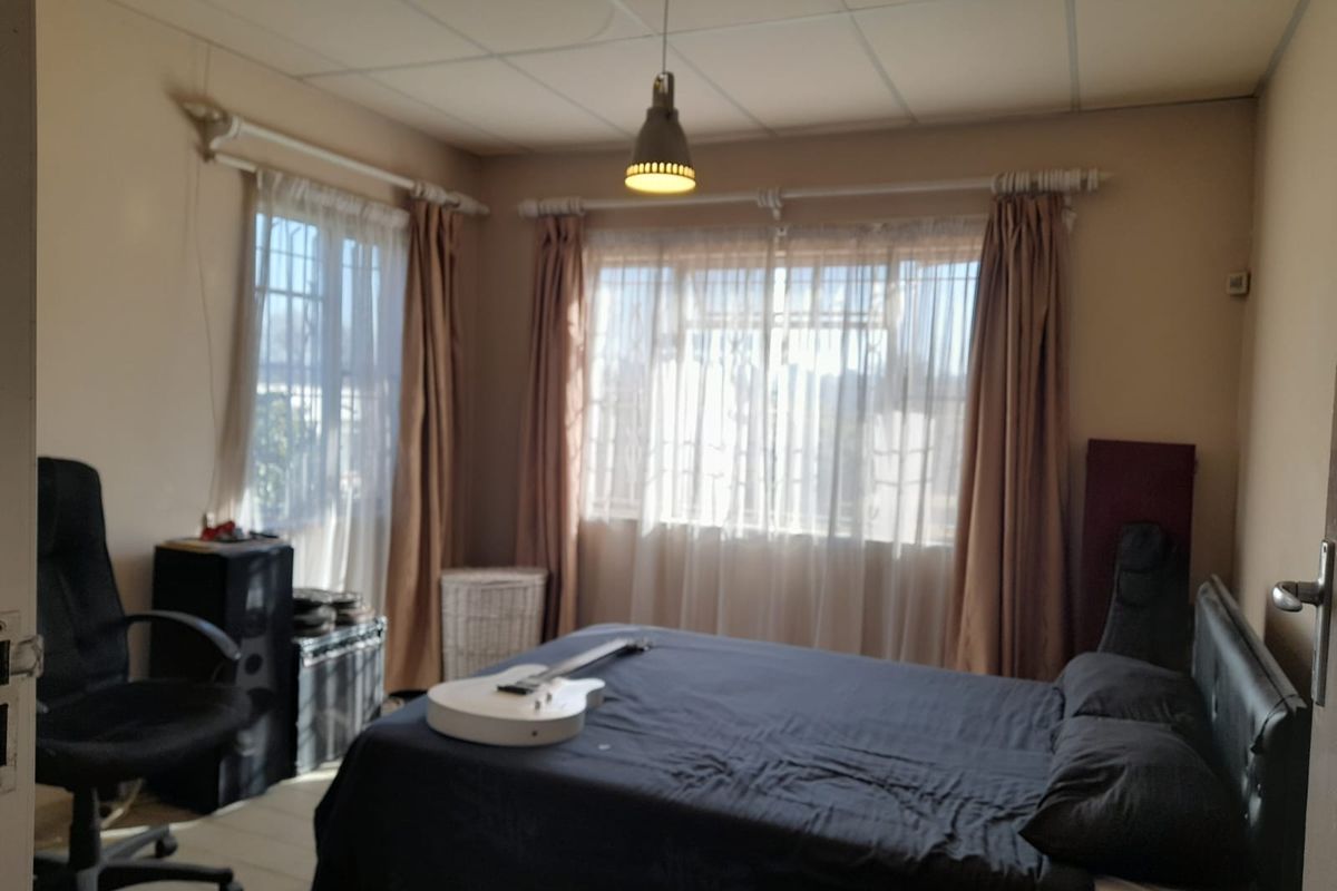 A bedroom featuring tiled flooring, security bars on the windows, and a drop ceiling with a central pendant light fixture.