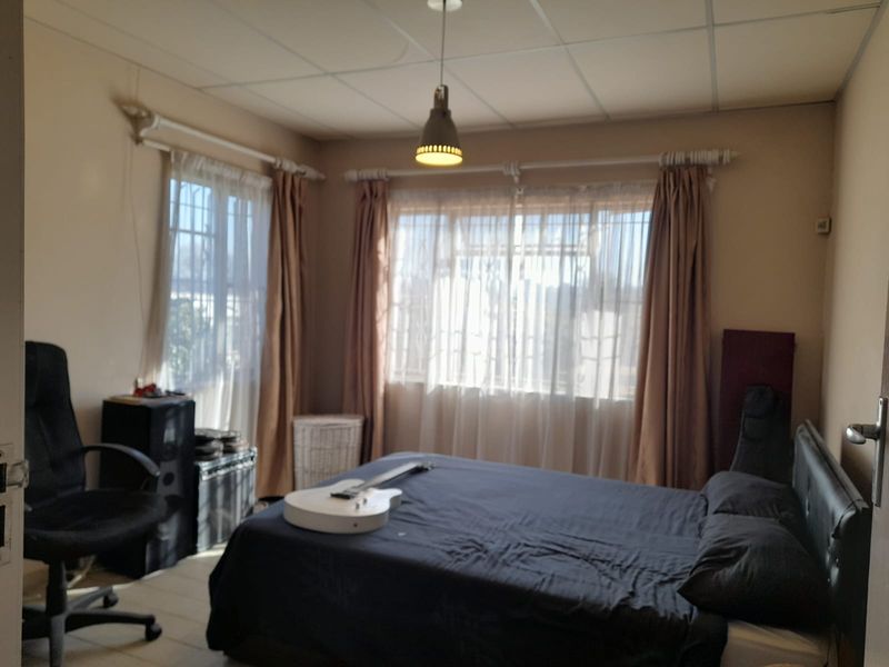 A bedroom featuring tiled flooring, security bars on the windows, and a drop ceiling with a central pendant light fixture.