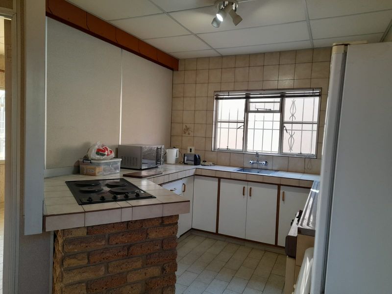 A functional kitchen featuring brick-based cabinetry, tiled countertops, a built-in electric hob, and a stainless steel sink with a tiled splashback.