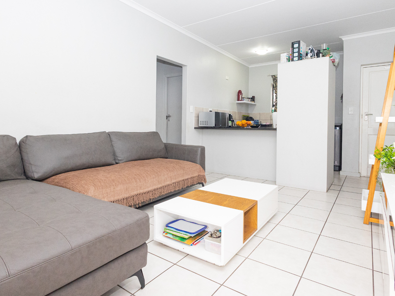 An open-plan living area featuring tiled flooring, a breakfast bar, and a functional kitchen layout, providing a versatile space for daily living.