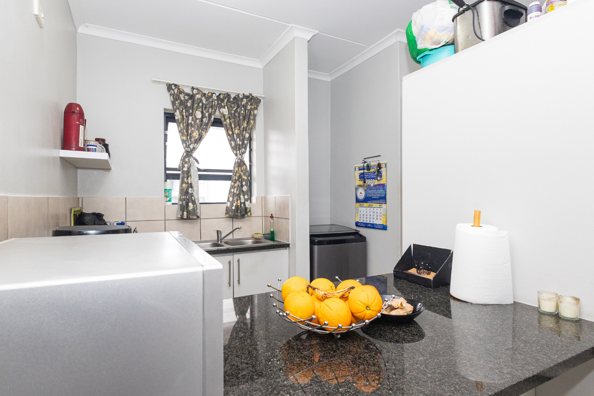 A functional kitchen featuring granite countertops, a double basin sink, and tiled backsplash with built-in cabinetry and coved cornices.