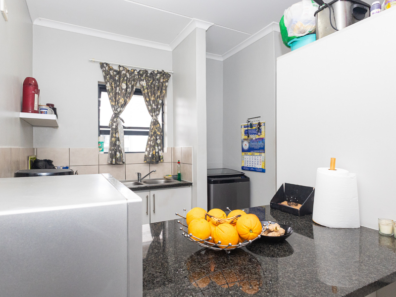 A functional kitchen featuring granite countertops, a double basin sink, and tiled backsplash with built-in cabinetry and coved cornices.