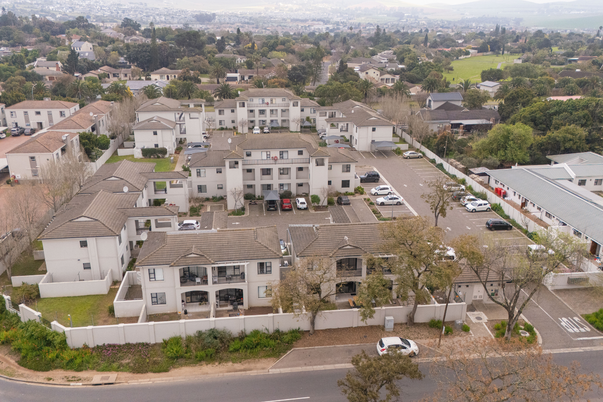 Aerial view of a residential apartment complex featuring multiple buildings, tiled roofs, paved parking areas, and perimeter boundary walls.