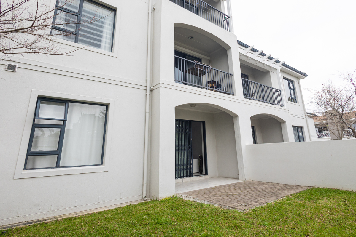 Rear view of the apartment building featuring a ground-level paved patio, upper-level balconies with metal railings, and well-maintained exterior finishes.