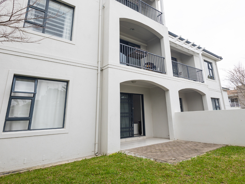 Rear view of the apartment building featuring a ground-level paved patio, upper-level balconies with metal railings, and well-maintained exterior finishes.
