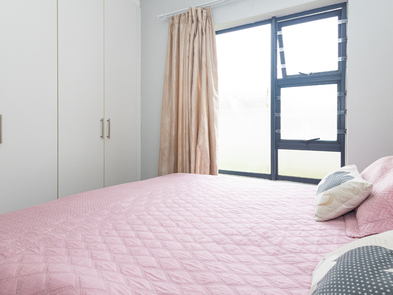A bedroom featuring built-in cupboards and a large window with aluminium frames, providing natural light to the space.