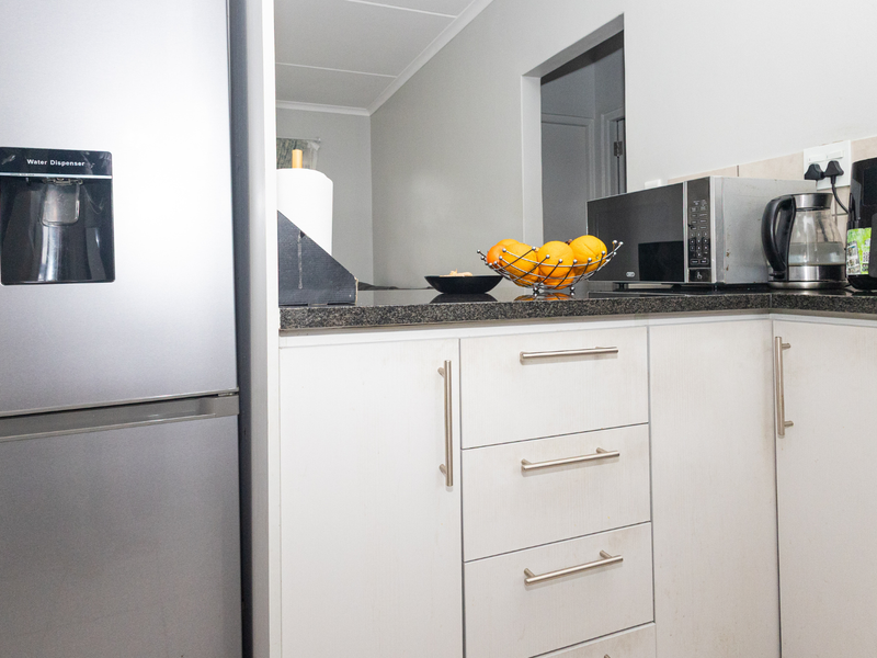 A functional kitchen area featuring white laminate cabinetry, dark granite countertops, and a modern stainless steel refrigerator.