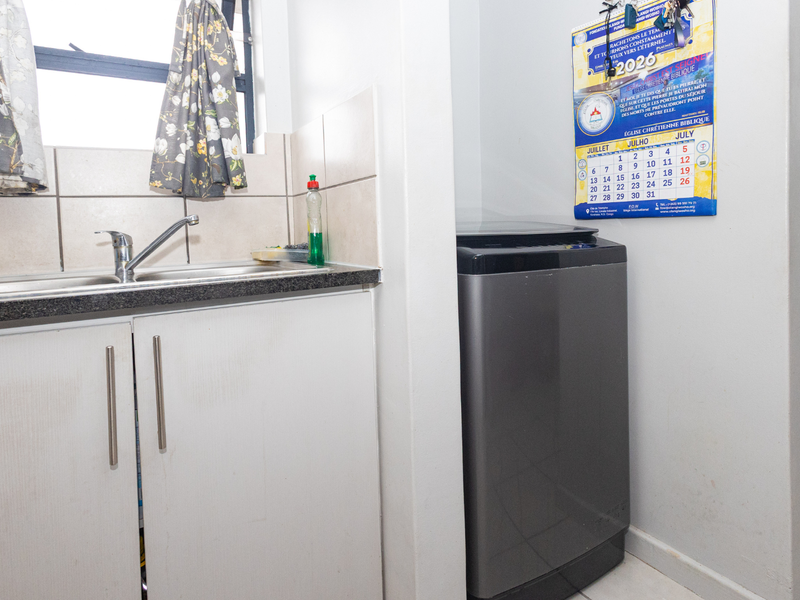 A functional laundry area featuring a stainless steel sink, tiled backsplash, and built-in cabinetry with space for a washing machine.