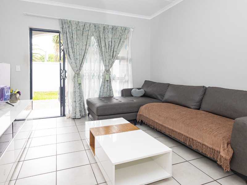 A bright living room featuring neutral tiled flooring and a sliding glass door providing direct access to the outdoor area.
