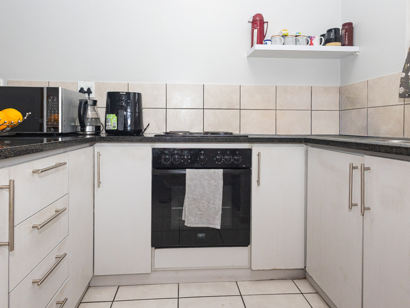 Compact kitchen featuring white cabinetry, granite countertops, tiled backsplash, and a built-in oven with electric hob.