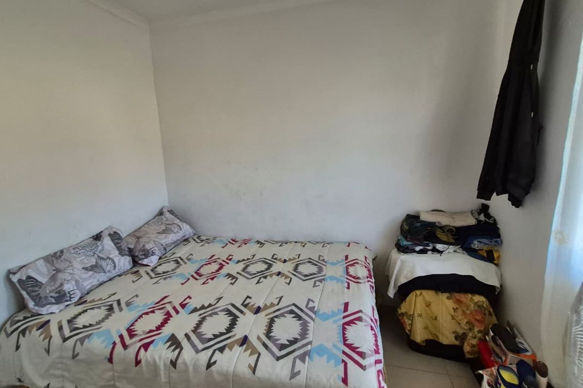 A compact bedroom featuring plain white walls and tiled flooring, offering a functional space that could benefit from cosmetic updates.