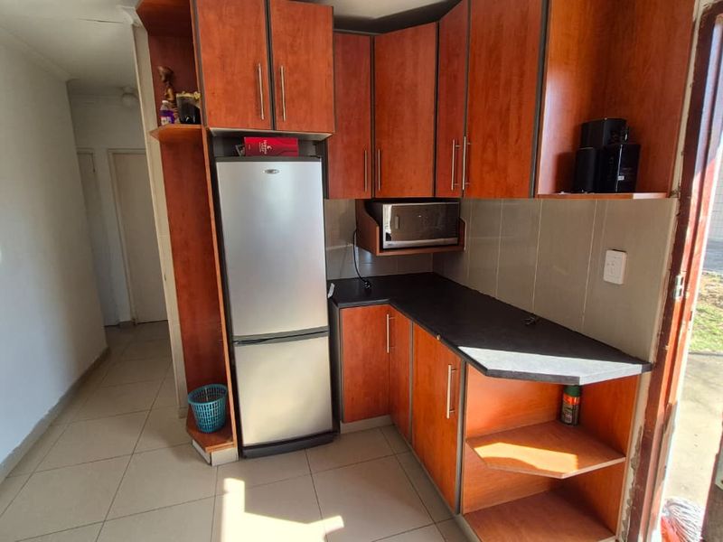 A compact kitchen featuring wood-look laminate cabinetry, tiled splashbacks, and tiled flooring, providing a functional prep area with direct outdoor access.