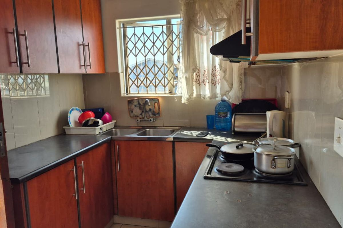 Compact kitchen featuring wood-look cabinetry, dark laminate countertops, a stainless steel double sink, and a built-in electric hob with an extractor fan.