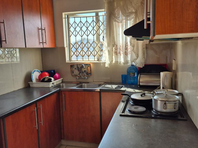 Compact kitchen featuring wood-look cabinetry, dark laminate countertops, a stainless steel double sink, and a built-in electric hob with an extractor fan.