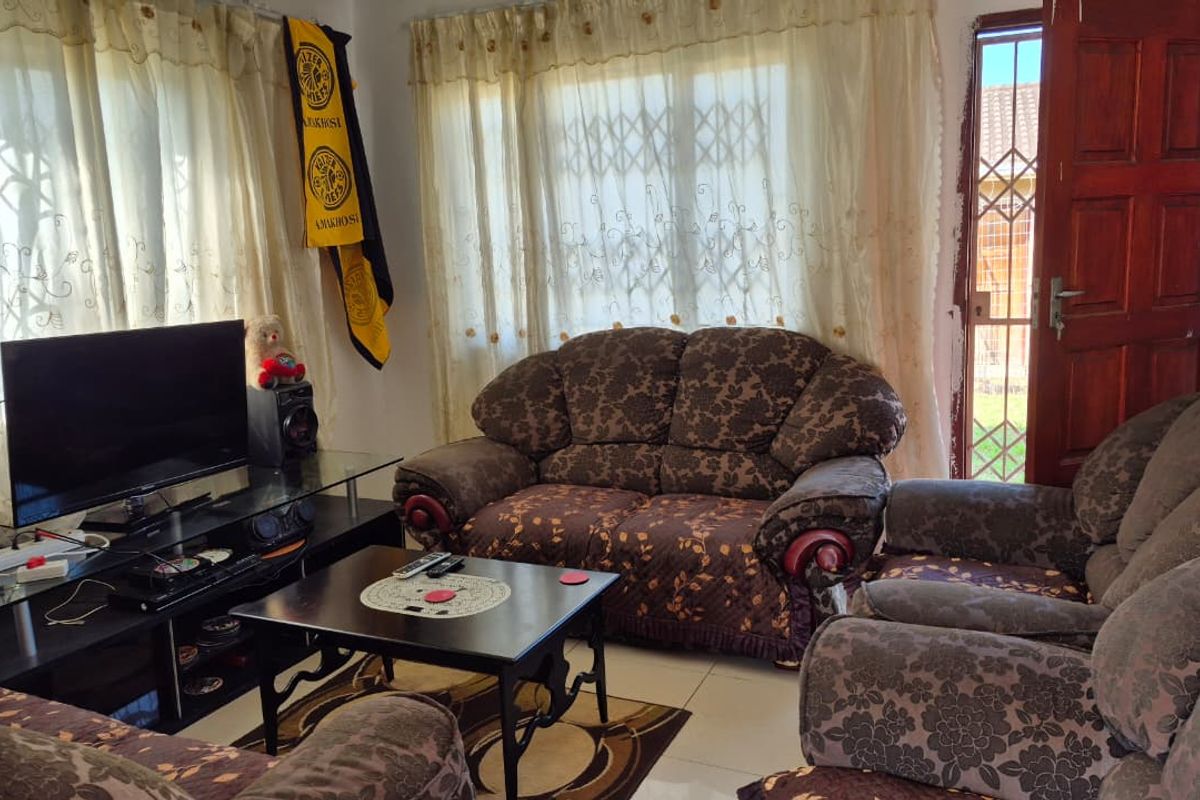 A living room featuring tiled flooring, a timber entrance door with a security gate, and large windows with curtains.