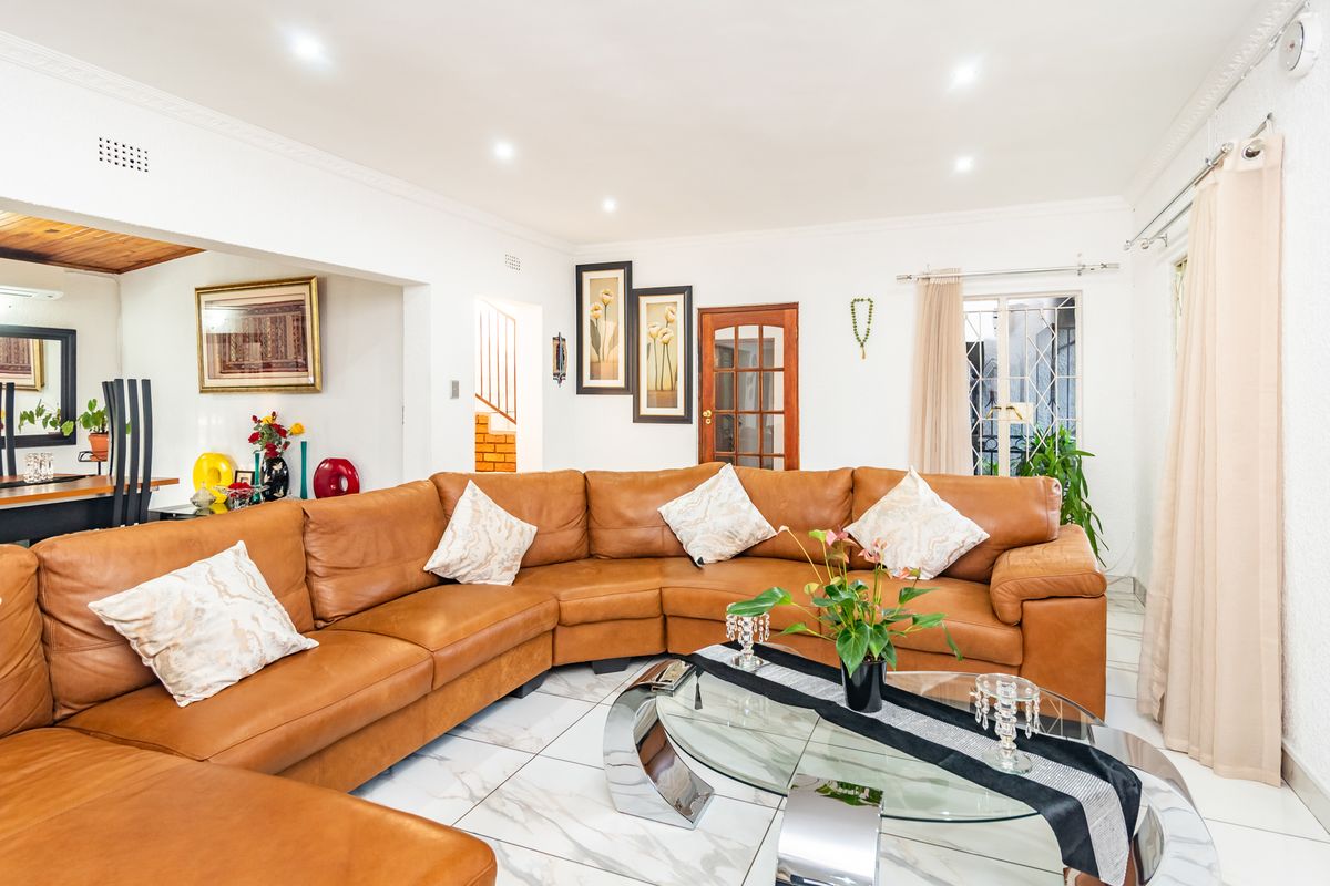A bright living room featuring white tiled flooring, recessed downlighting, and crown molding, with an open-plan layout connecting to adjacent living spaces.